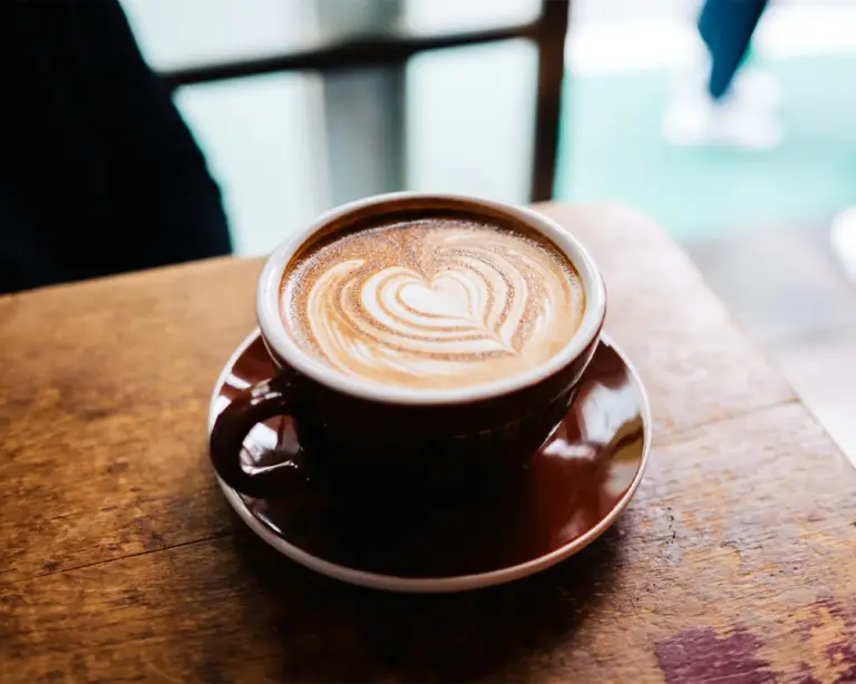 A freshly brewed cup of coffee topped with delicate latte art, featuring a smooth, creamy foam pattern swirling across the surface.
