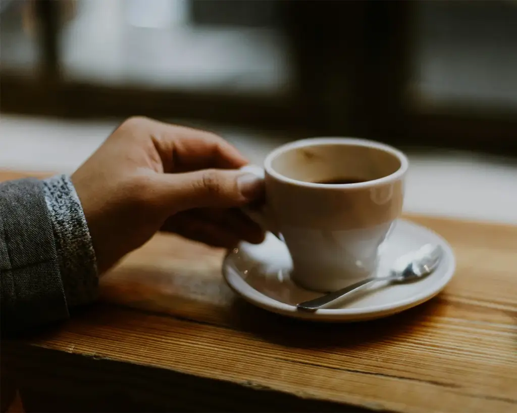 A close-up of a hand gently holding a warm cup of coffee, with soft lighting and a blurred café background that highlights the comforting and relaxing moment of enjoying a hot drink.