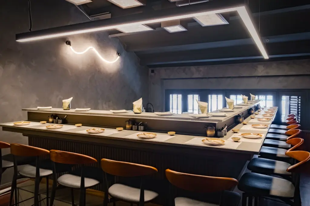 Modern minimalist interior of Toku Nori on Telok Ayer Street, Singapore, featuring a sleek U-shaped bar, neon lighting, and concrete walls. Trendy handroll and wagyu dining spot for locals