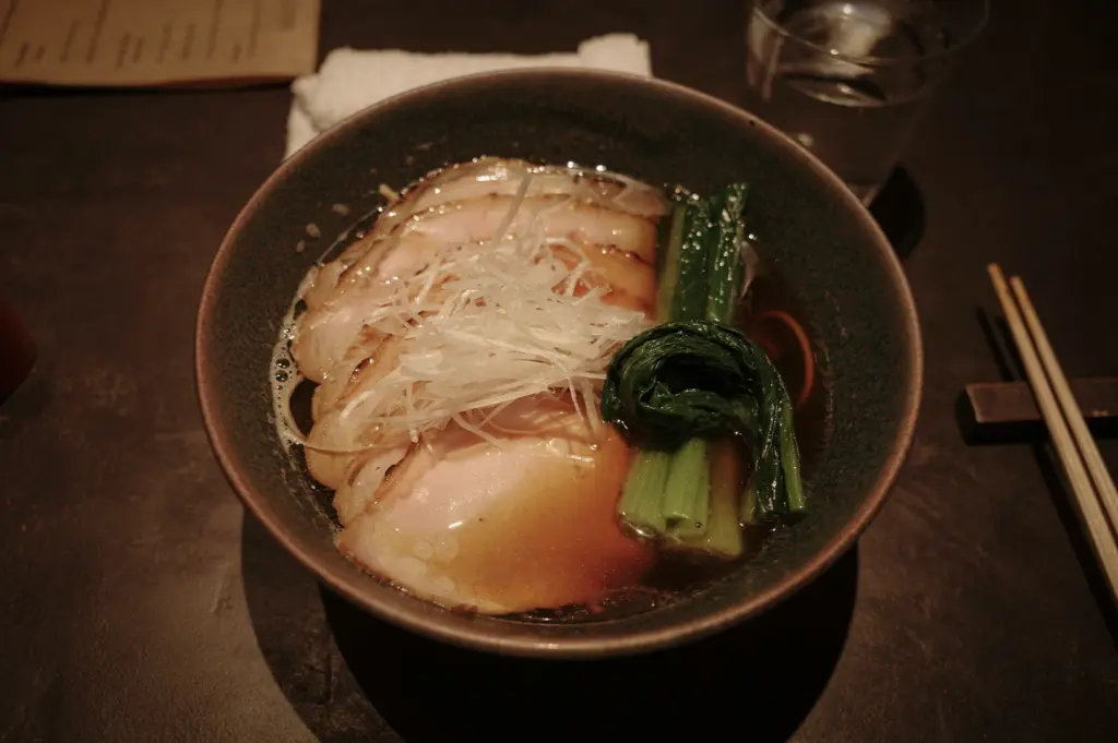 Top-down view of shoyu ramen in a Japanese bowl featuring sliced pork, noodles, and assorted vegetables in a rich soy-based broth, with chopsticks placed beside the bowl, styled as clean, high-detail food photography.