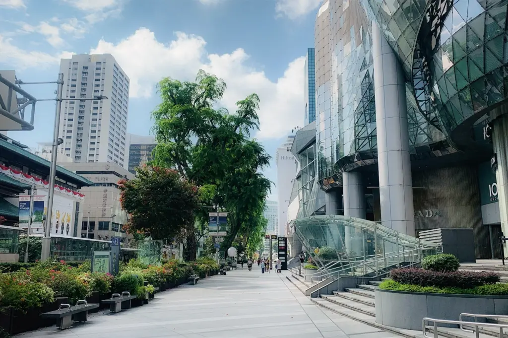 View of Orchard Road featuring lush greenery, modern glass high rise buildings, and a vibrant urban shopping district with tree-lined streets and contemporary architecture, captured in a clean, high-detail cityscape.