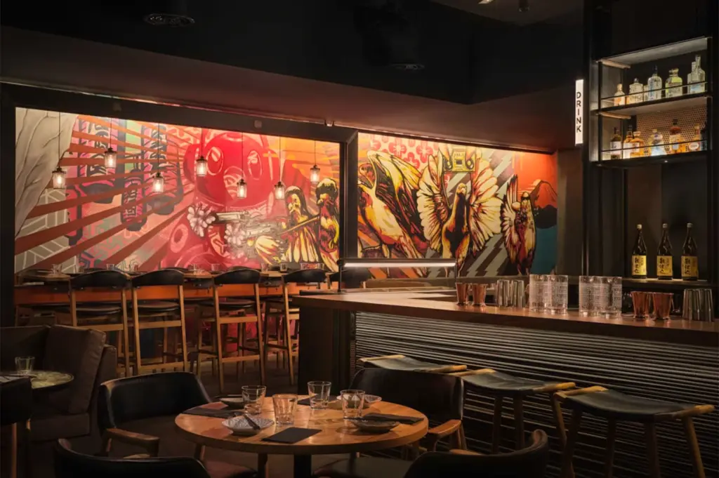 Modern interior of Neon Pigeon on Keong Saik Road featuring vibrant street art murals, industrial bar seating, and a moody urban atmosphere. Trendy Japanese social house and cocktail bar in Singapore.