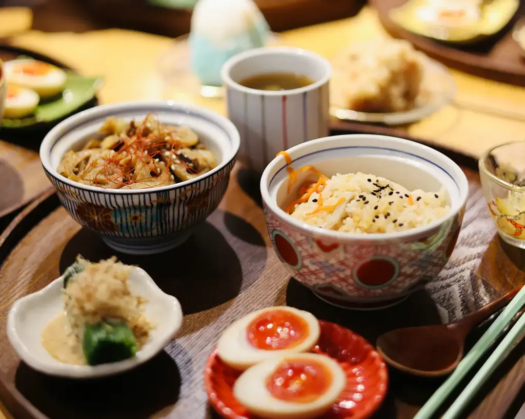 A vibrant meal with diverse Japanese dishes on wooden trays, featuring rice bowls, pickled vegetables, and eggs.