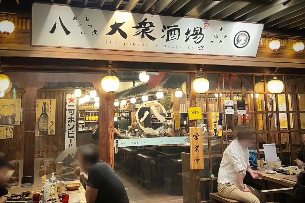 The Public Izakaya storefront on Tras Street, Singapore, with traditional wooden architecture, glowing lanterns, and diners. Authentic Japanese tavern atmosphere for nightlife and dining