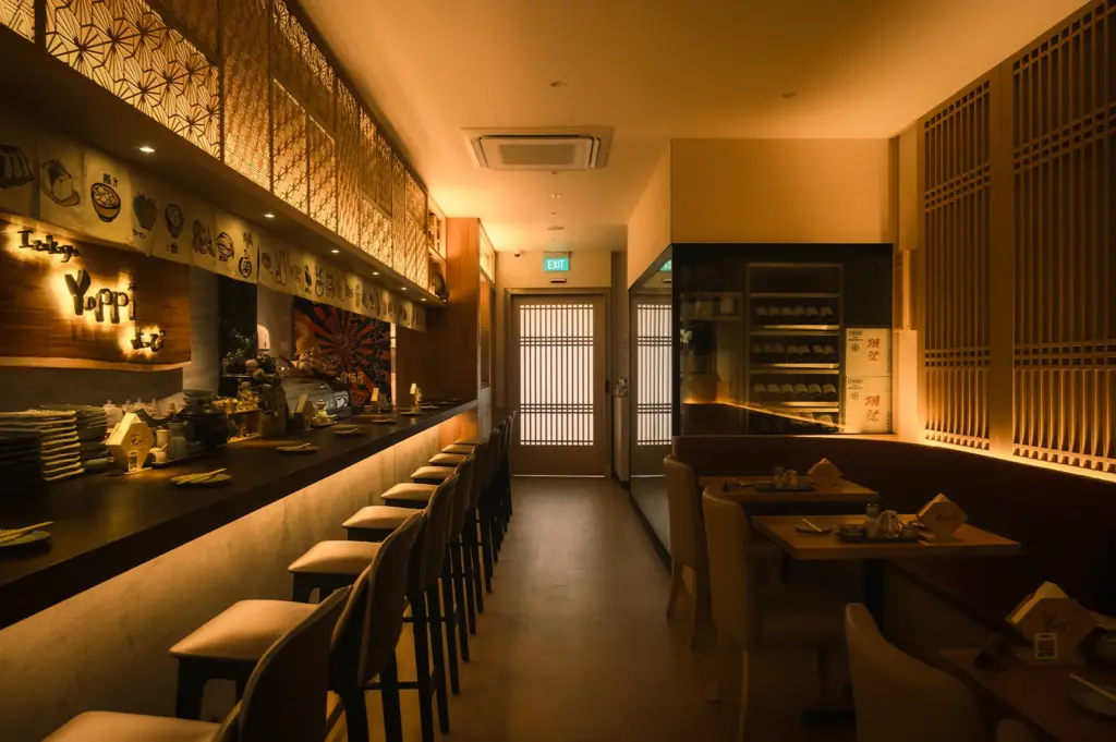 Warmly lit interior of Izakaya Yoppi on Neil Road, Singapore, featuring elegant wood latticework, a sleek bar counter, and cozy booth seating. Authentic Japanese restaurant design for locals