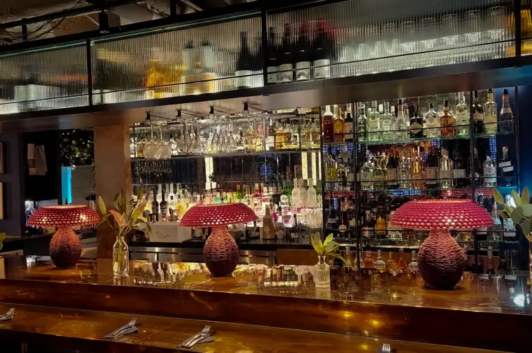 Elegant bar interior at Wild Honey Mandarin Singapore featuring illuminated shelves of spirits, marble countertop seating and decorative red table lamps in a modern dining setting