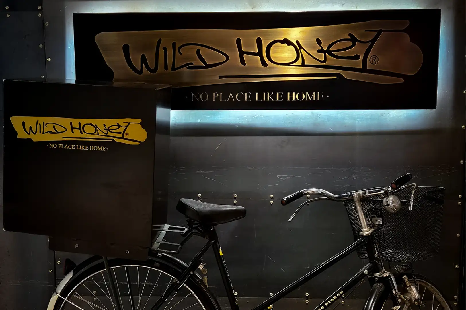 Vintage delivery bicycle display at Wild Honey Mandarin Singapore featuring branded cargo box and illuminated restaurant sign with industrial-style interior decor