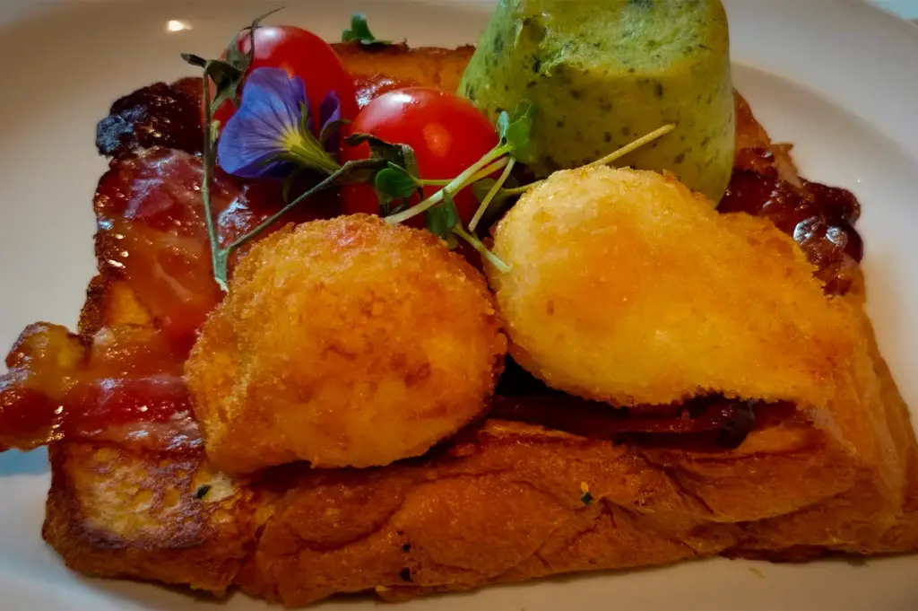 Gourmet brunch toast at Wild Honey Mandarin Singapore topped with crispy croquettes, bacon, avocado mousse and fresh greens served on toasted brioche bread