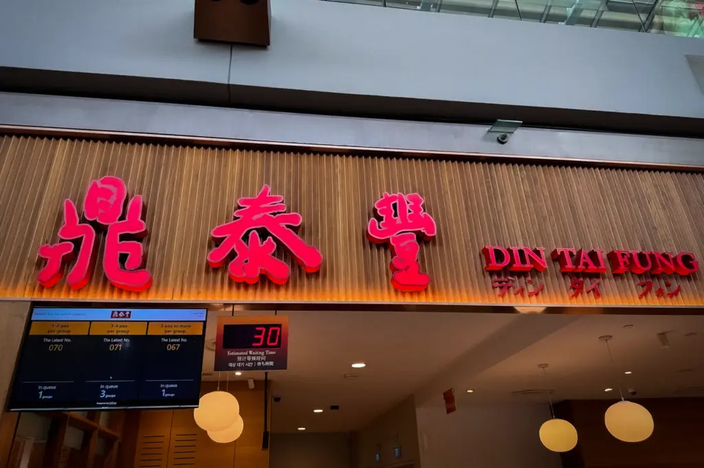 Din Tai Fung Singapore storefront with bright red Chinese signage, queue display screen, and modern restaurant entrance inside a shopping mall dining area