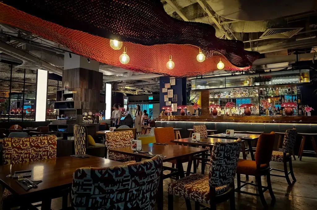 Stylish dining interior at Wild Honey Mandarin Singapore featuring patterned seating, ambient lighting, artistic ceiling decor and a modern bar area in a cozy restaurant setting
