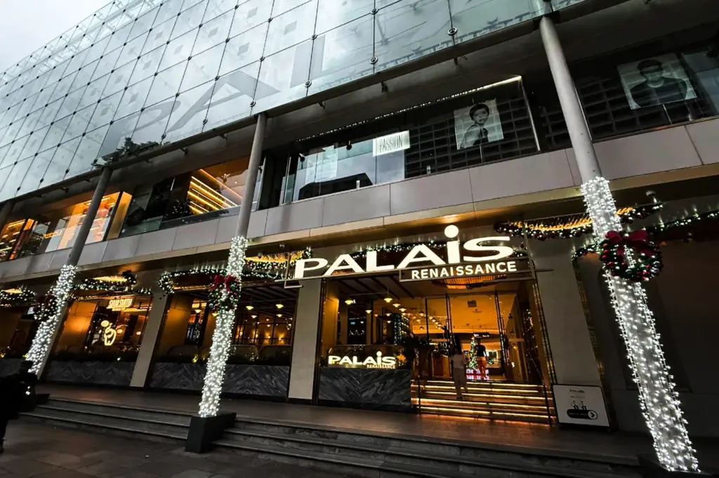 A vibrant night shot of the modern, glass-paneled storefront for "Bacha Coffee" at ION Orchard, featuring glowing amber grid lighting and luxury store interiors visible through large windows.