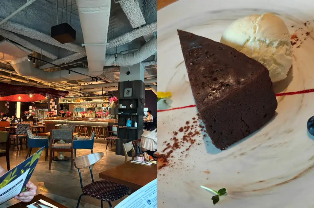 A side-by-side split composition captures a trendy restaurant interior and a close-up of a plated dessert, representing the file "5-The Five Best Dessert Shops in Orchard.webp". The left panel shows an eye-level view of a spacious, dimly lit dining room featuring an industrial-style ceiling with exposed pipes, scattered wooden tables paired with multi-colored upholstered chairs, and a long bar counter softly glowing in the background under warm red pendant lights. The right panel shifts to a close-up shot of a thick, triangular slice of dense dark chocolate cake or brownie served on a marbled white plate alongside a scoop of vanilla ice cream, elegantly finished with a fine dust of cocoa powder, a thin drizzle of red berry sauce, and a tiny green garnish.